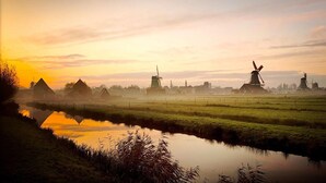 Een vredig landschap met windmolens, een kalme rivier en een mistige lucht.