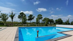 Een rechthoekig buitenzwembad met een helder blauw wateroppervlak, omringd door een betegeld zonnedek.