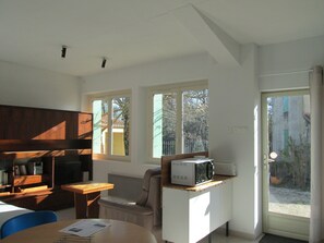 Eine kleine Küche mit einer Mikrowelle auf einer Arbeitsplatte, einem Holztisch, einem Stuhl und einem Fenster mit Blick auf Bäume und einen Zaun.
