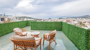 A rooftop terrace with wicker furniture and a green hedge wall, overlooking a cityscape. - Vila Myrtaj (Ksamil)