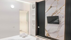 A modern hotel room with a bed, a TV, and a marble wall. - Vila Myrtaj (Ksamil)