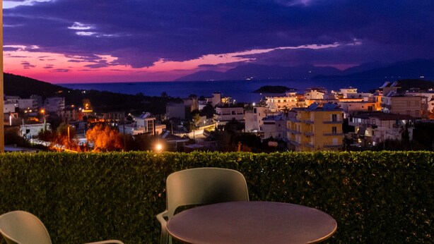 An outdoor seating area with chairs and a table, overlooking a cityscape at dusk. - Vila Myrtaj (Ksamil)