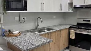 Una cocina con encimera de granito, pileta de acero inoxidable, muebles de madera, microondas y estufa.