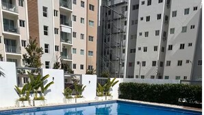 Una piscina rodeada por un muro blanco con plantas, con edificios residenciales de varios pisos al fondo.