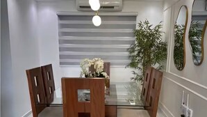 Un comedor con una mesa de vidrio, sillas de madera, una lámpara colgante y una planta en maceta.