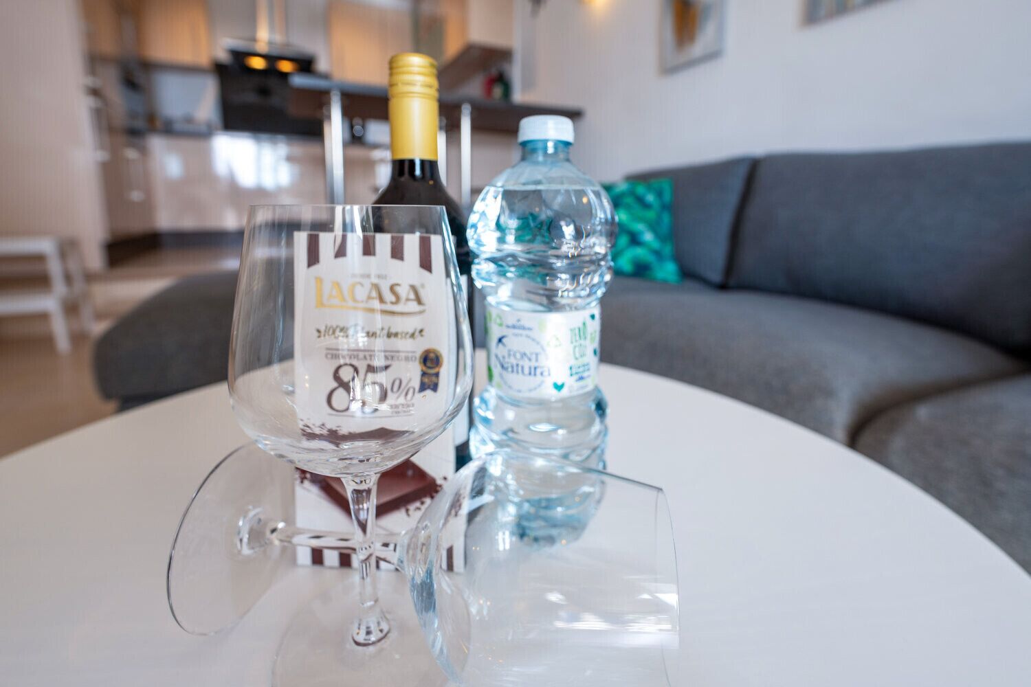 Una copa de vino, una botella de vino chocolate Lacasa y una botella de agua sobre una mesa en una sala de estar.