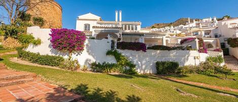 A white building with a stone wall, steps leading up to it, and a clear blue sky.