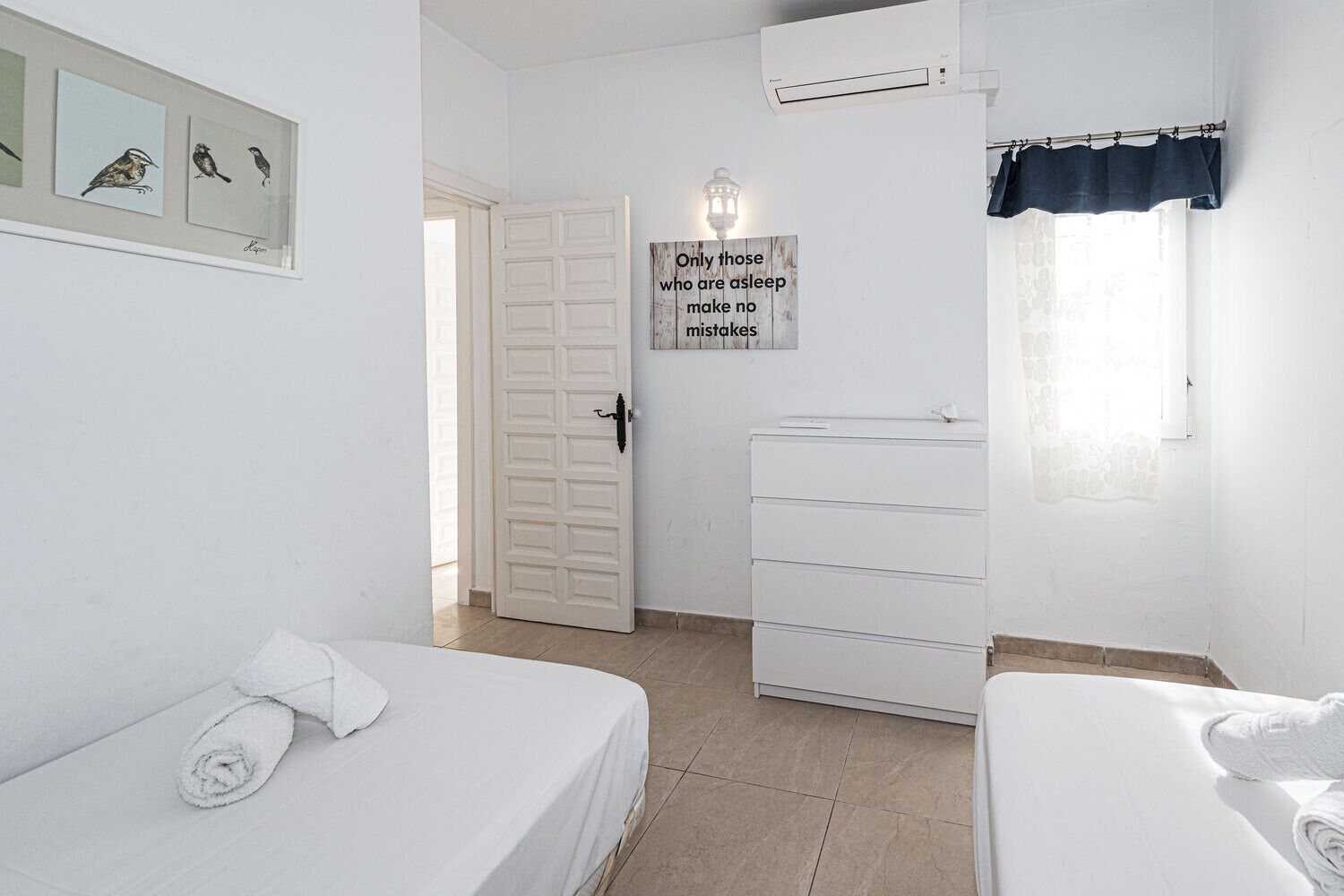 Una habitación con dos camas, un armario, una puerta y aire acondicionado instalado en la pared.