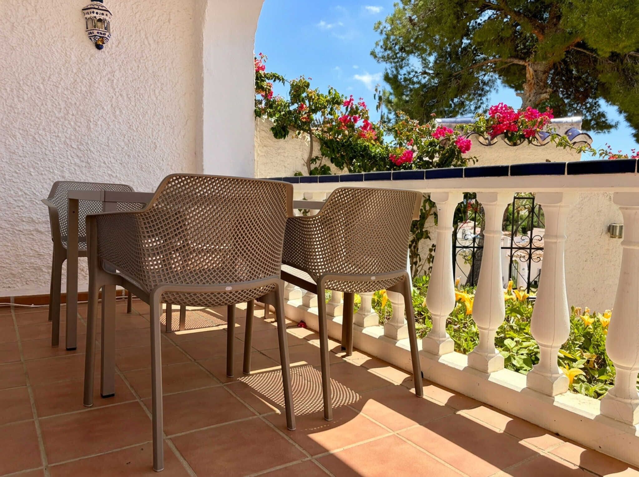 An outdoor patio with wicker furniture, a white balustrade, and flowering plants.