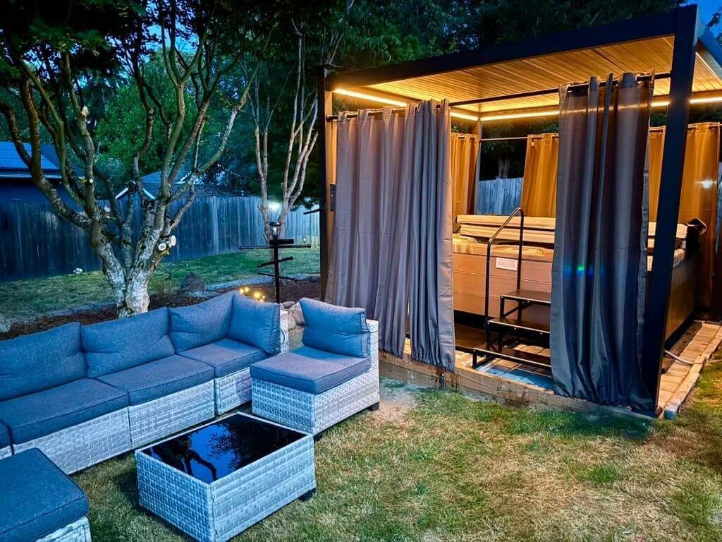 An outdoor seating area with a sofa and a coffee table, a covered patio with curtains, and a wooden deck.
