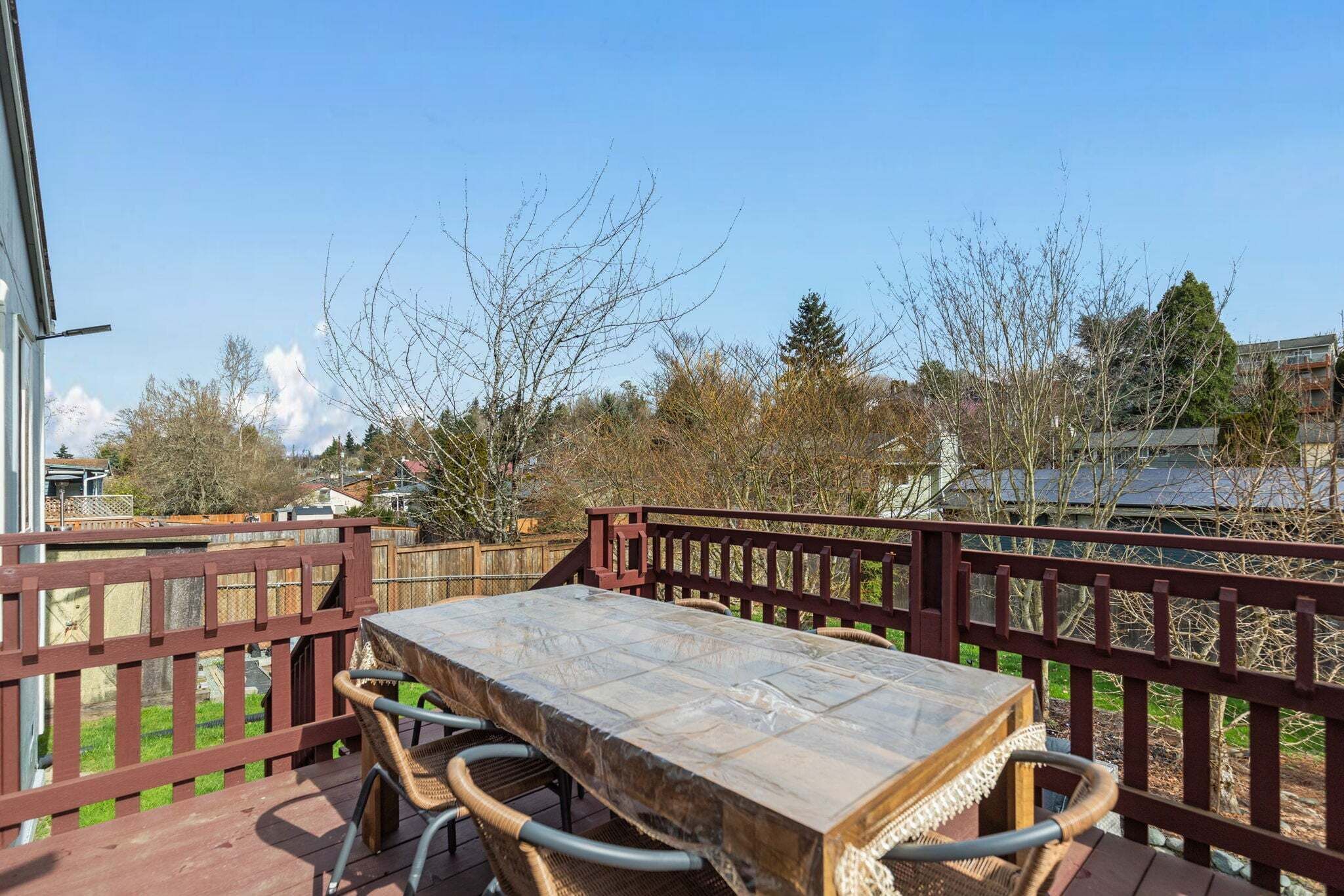 A wooden deck with a table and chairs, a red railing, and a view of trees and buildings.