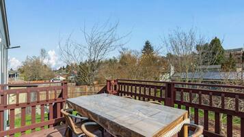 A wooden deck with a table and chairs, a red railing, and a view of trees and buildings.