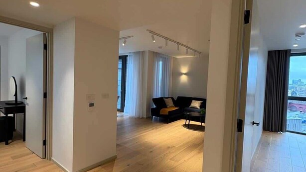 A spacious living area with a wooden floor, a black sofa, and a dining table.