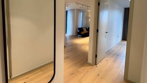 A modern interior with a large mirror, wooden flooring, and a hallway leading to a living area with a sofa.