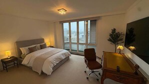 Habitación de hotel con cama, escritorio, silla, lámpara, ventana con persianas y un cuadro en la pared.