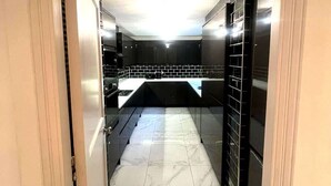 Un pasillo estrecho que conduce a una cocina con gabinetes negros, una encimera blanca y piso de baldosas.