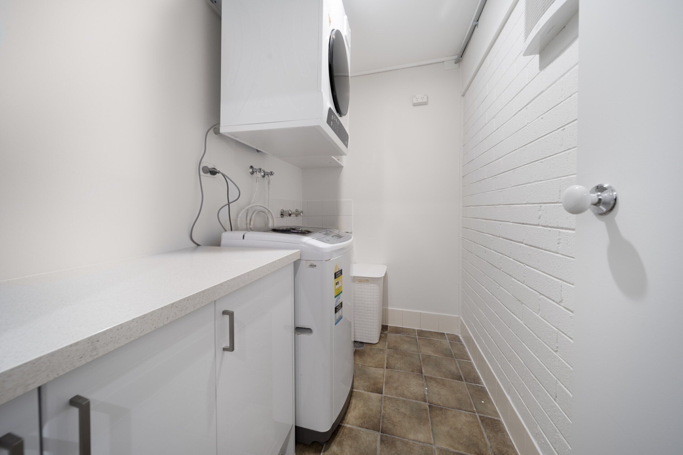 A laundry area with a washing machine, dryer, and a trash bin.