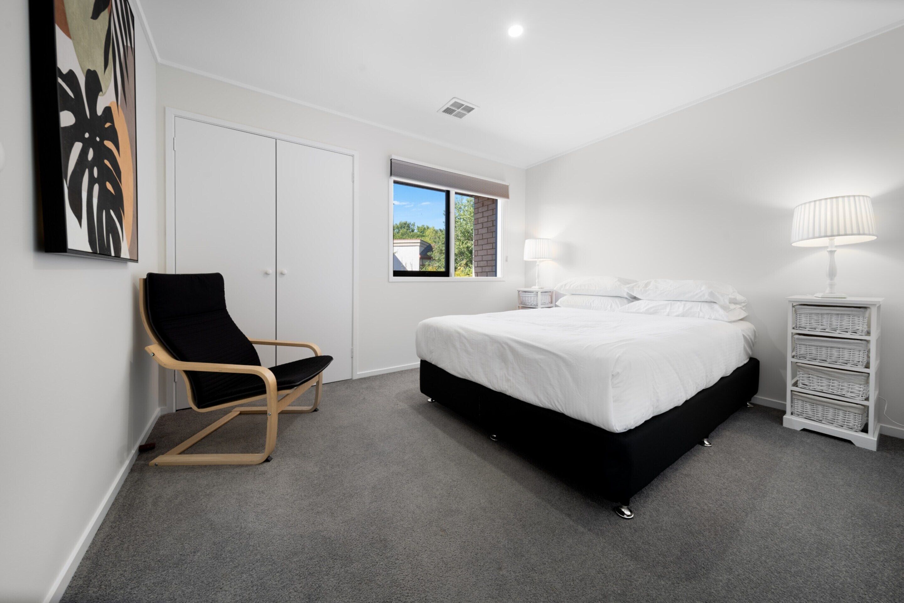 A bedroom with a bed, a chair, a lamp, a wardrobe, and a window.