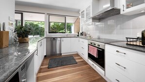 Una cucina moderna con mobili bianchi, elettrodomestici in acciaio inossidabile, un piano di lavoro nero e vista sul verde.