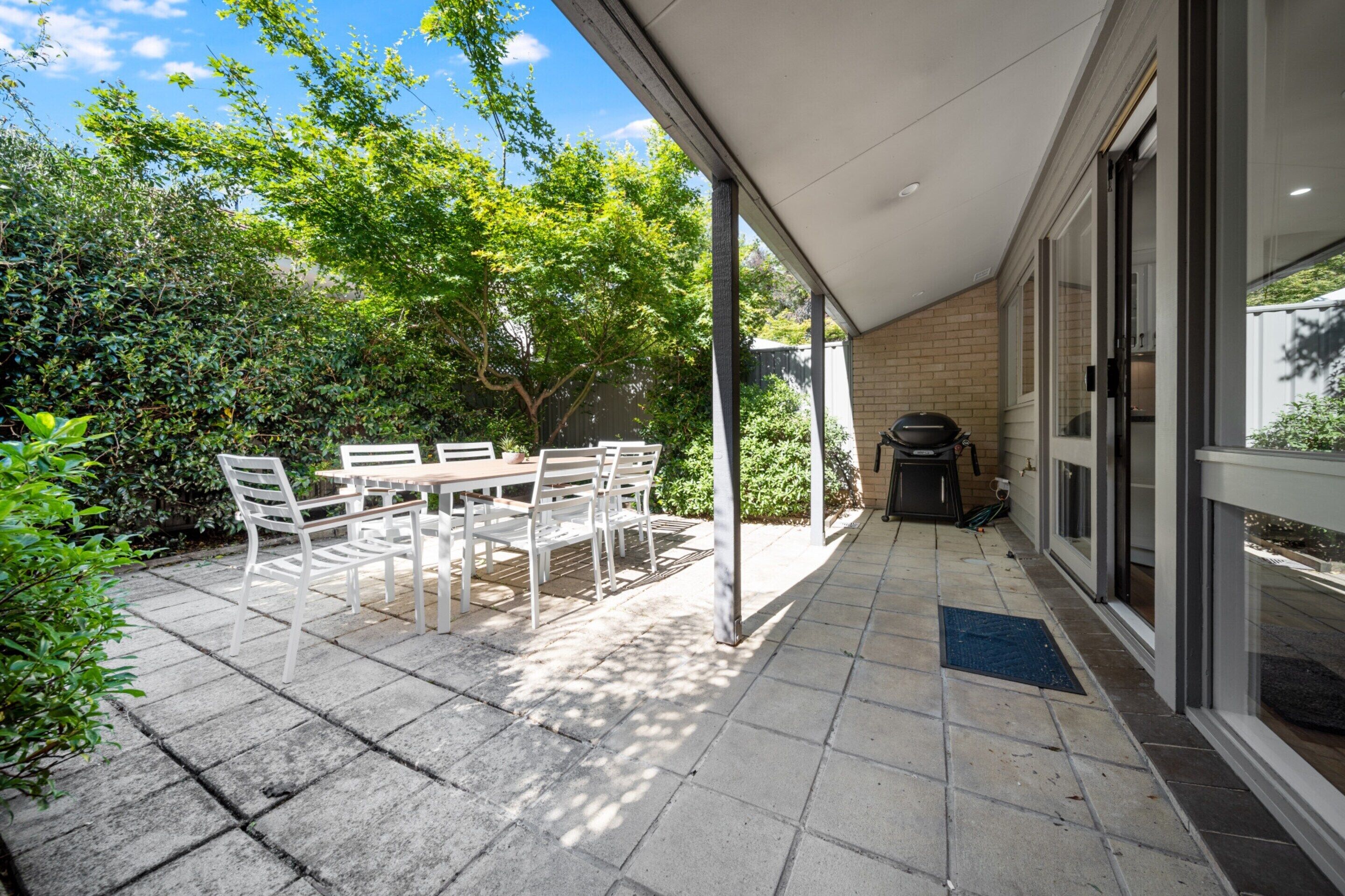 A covered patio with a table and chairs, a barbecue grill, and a view of the garden.
