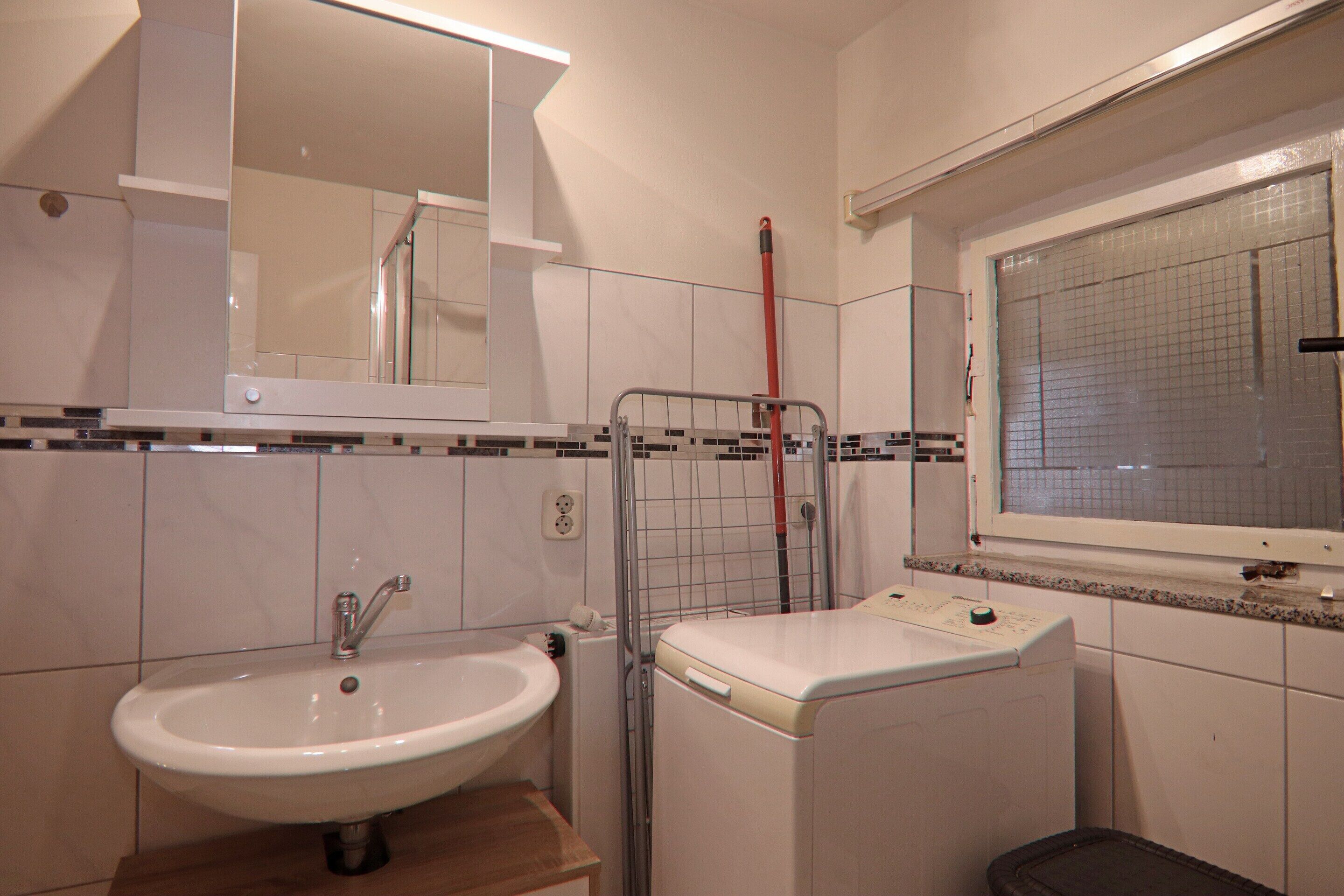 Ein Badezimmer mit Waschbecken, Spiegel, Fenster und Waschmaschine.