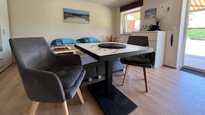 A dining area with a table, chairs, and a sofa with cushions. - Charmante Ferienwohnung mit Grill in Rakow (Am Salzhaff)