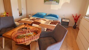 A bedroom with a bed, two nightstands, a dresser, a chair, a table with a basket, and a painting on the wall. - Charmante Ferienwohnung mit Grill in Rakow (Am Salzhaff)