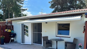 A small building with a covered patio, a sliding door, and a window overlooking a body of water. - Charmante Ferienwohnung mit Grill in Rakow (Am Salzhaff)
