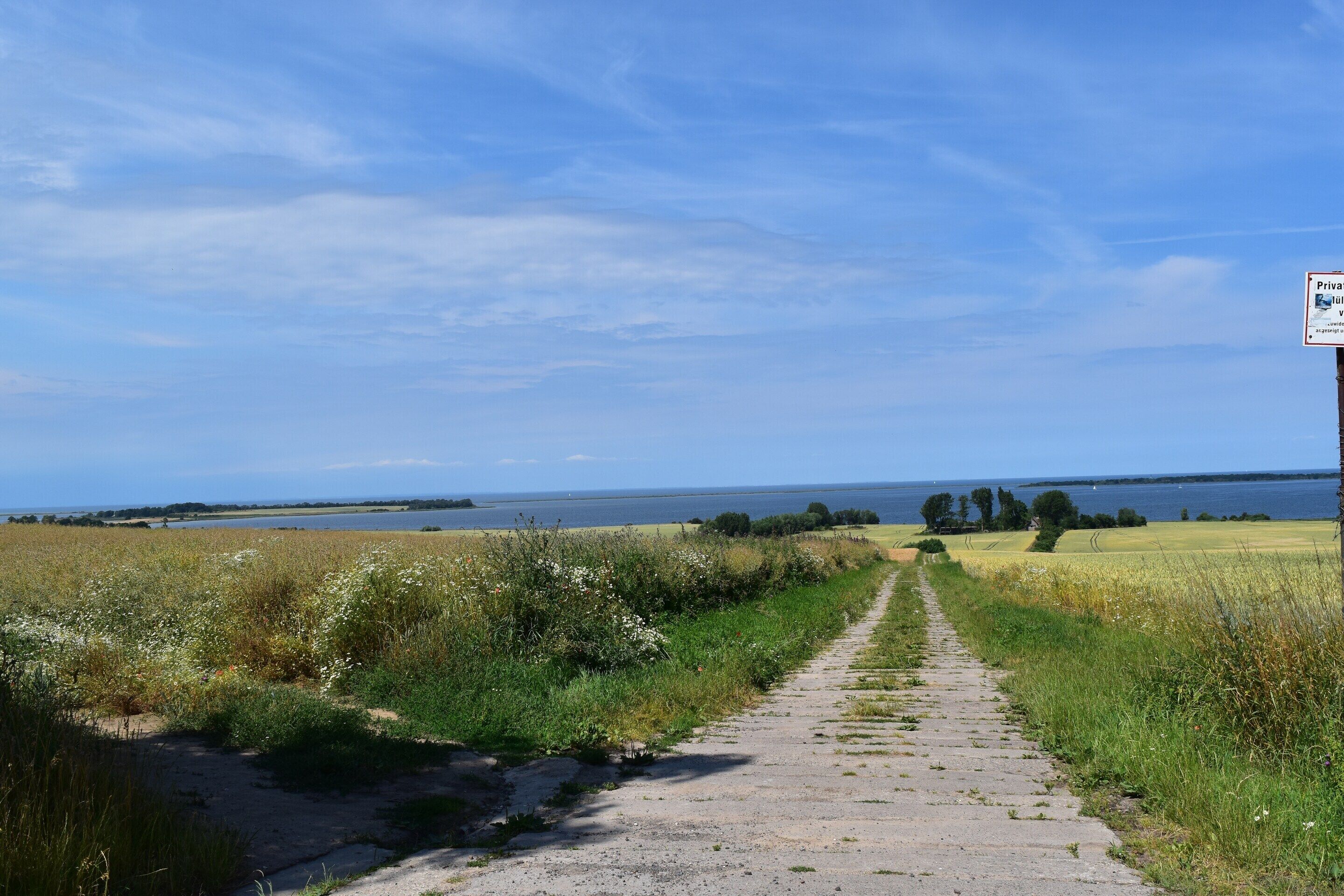 A rural pathway leading to a body of water with a sign indicating private property.