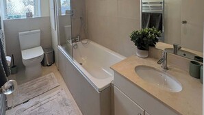 Un baño moderno con bañera, inodoro, lavamanos y un espejo grande.