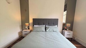 Una cama grande con cabecera gris, dos mesitas de noche con lámparas y un espejo en la pared.