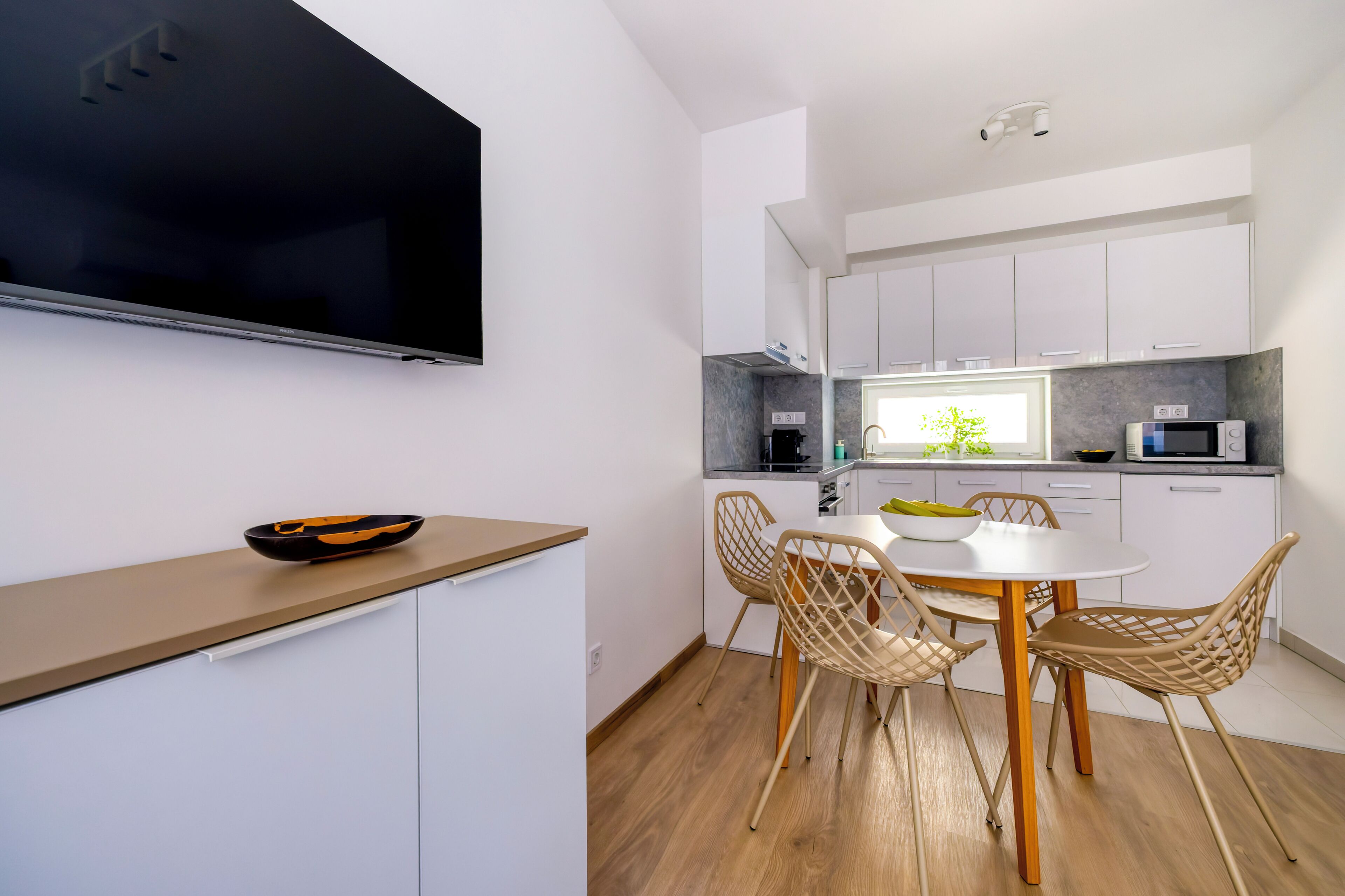 Una cocina moderna con armarios blancos, un televisor de pantalla plana, una mesa de comedor con sillas y un microondas.