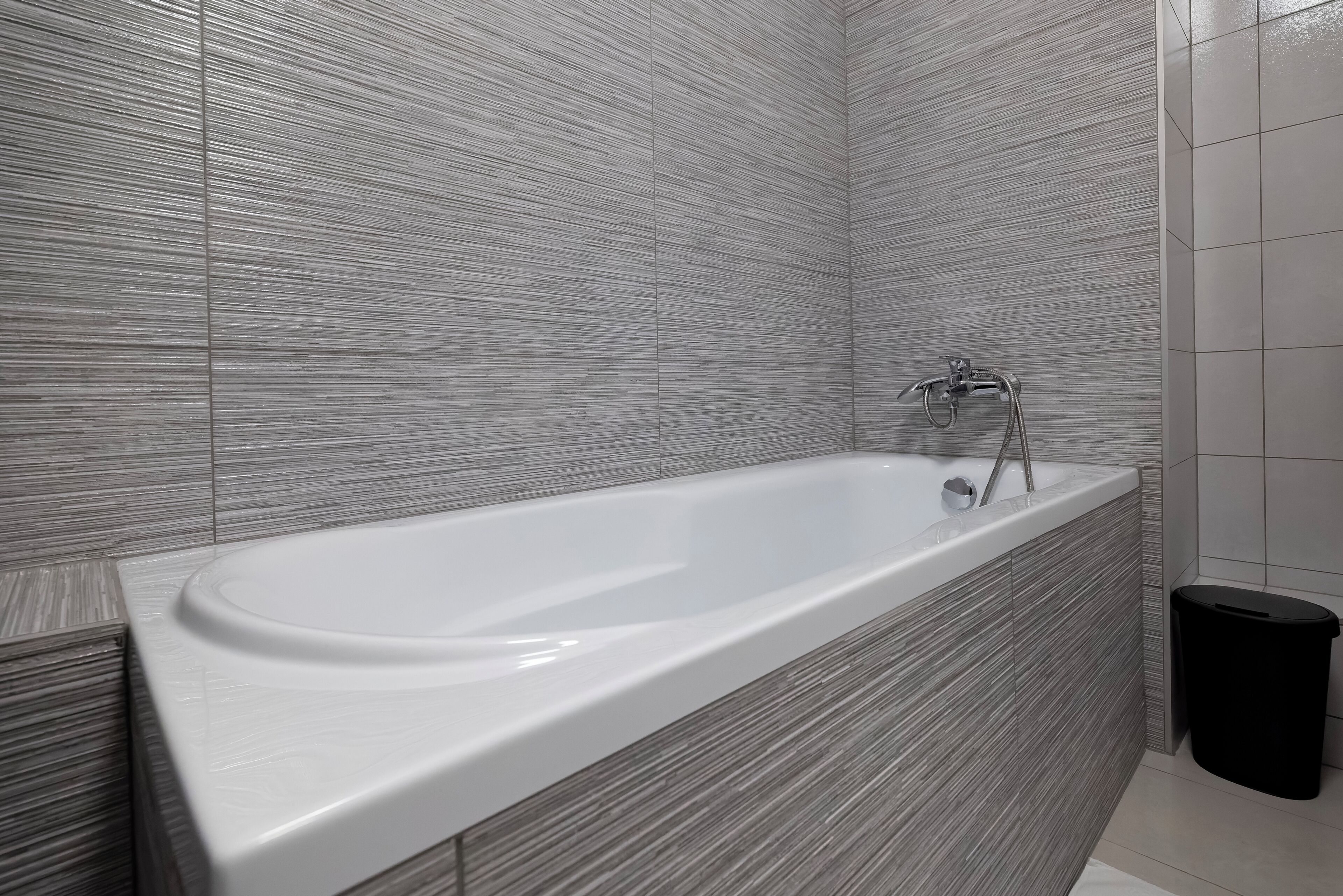 Ein modernes Badezimmer mit freistehender Badewanne, gefliesten Wänden und einem schwarzen Mülleimer.