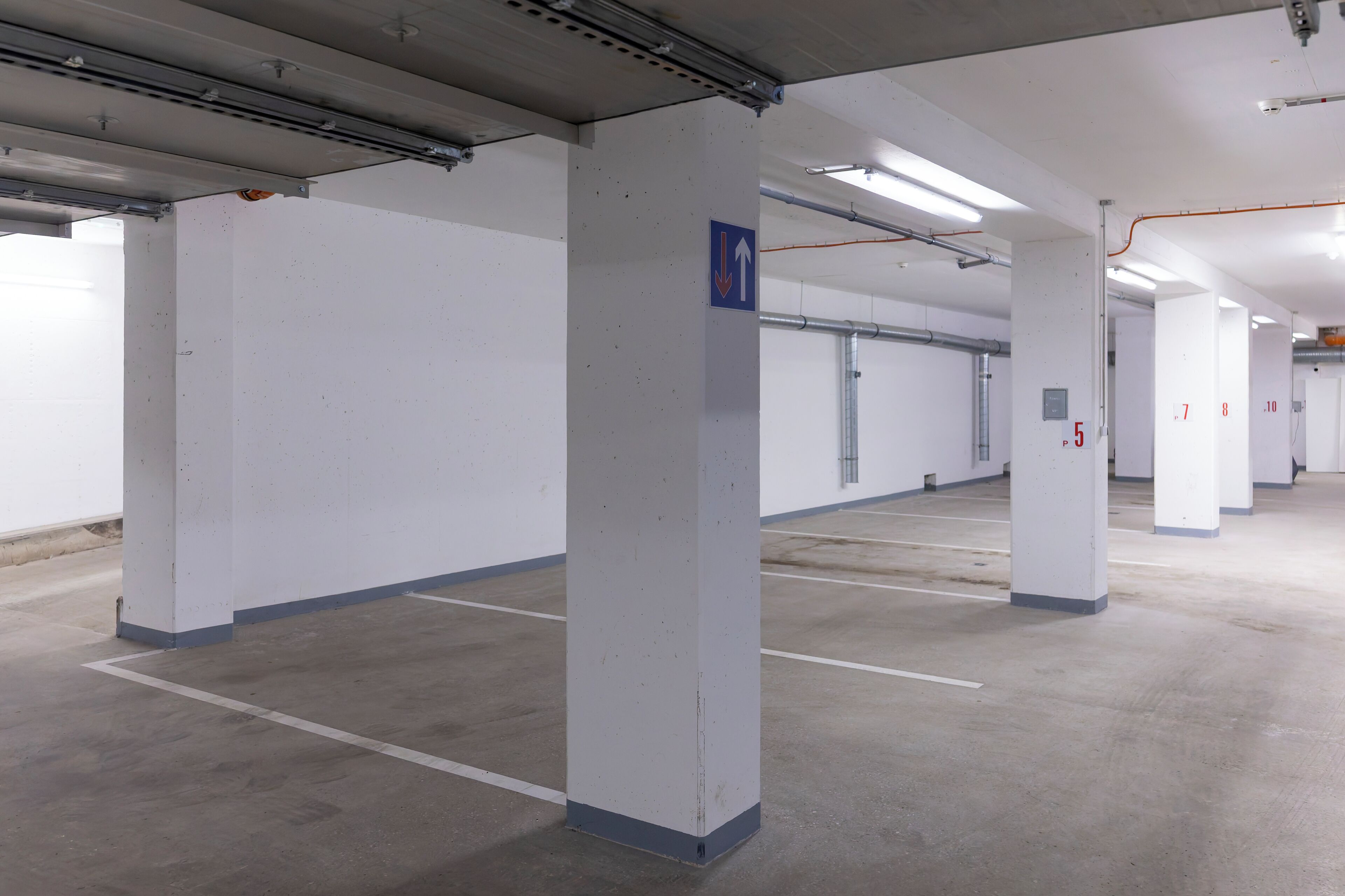 Un parking avec des piliers blancs, des flèches indiquant la direction et des places de stationnement numérotées.