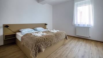 A bedroom with a bed, a bedside table, a window with curtains, and a radiator.