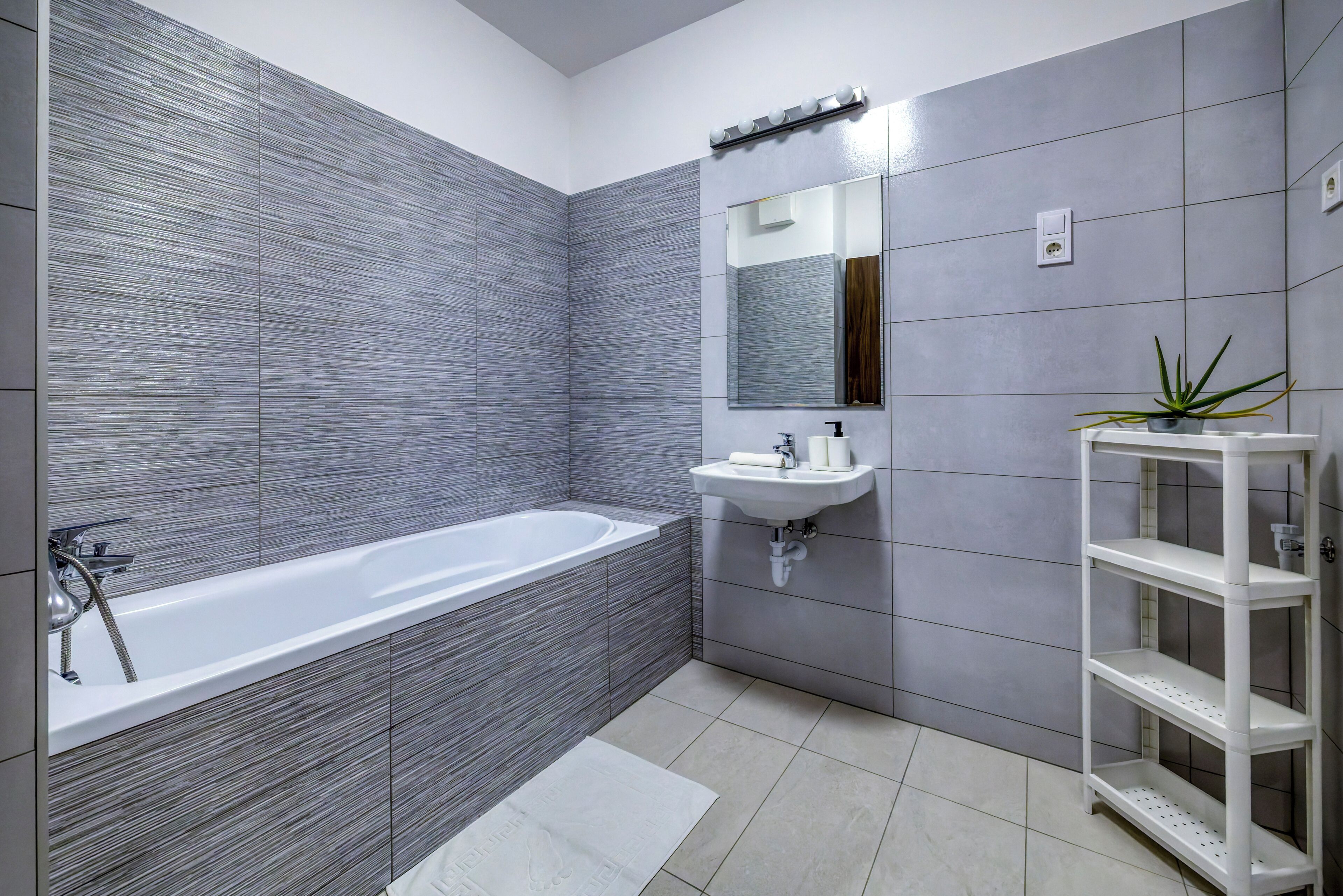 Un baño moderno con bañera, lavamanos, espejo y estantería.