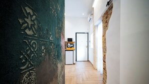 Een hal met een visgraatvloer, een bakstenen muur en een deur, met op de achtergrond een kleine kitchenette.