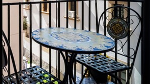 Een balkon met een ronde tafel en stoelen, een hekwerk en een gebouw op de achtergrond.