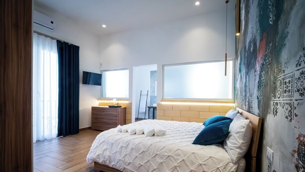Een moderne slaapkamer met een groot bed, nachtkastjes, een dressoir en een tv die aan de muur is bevestigd.