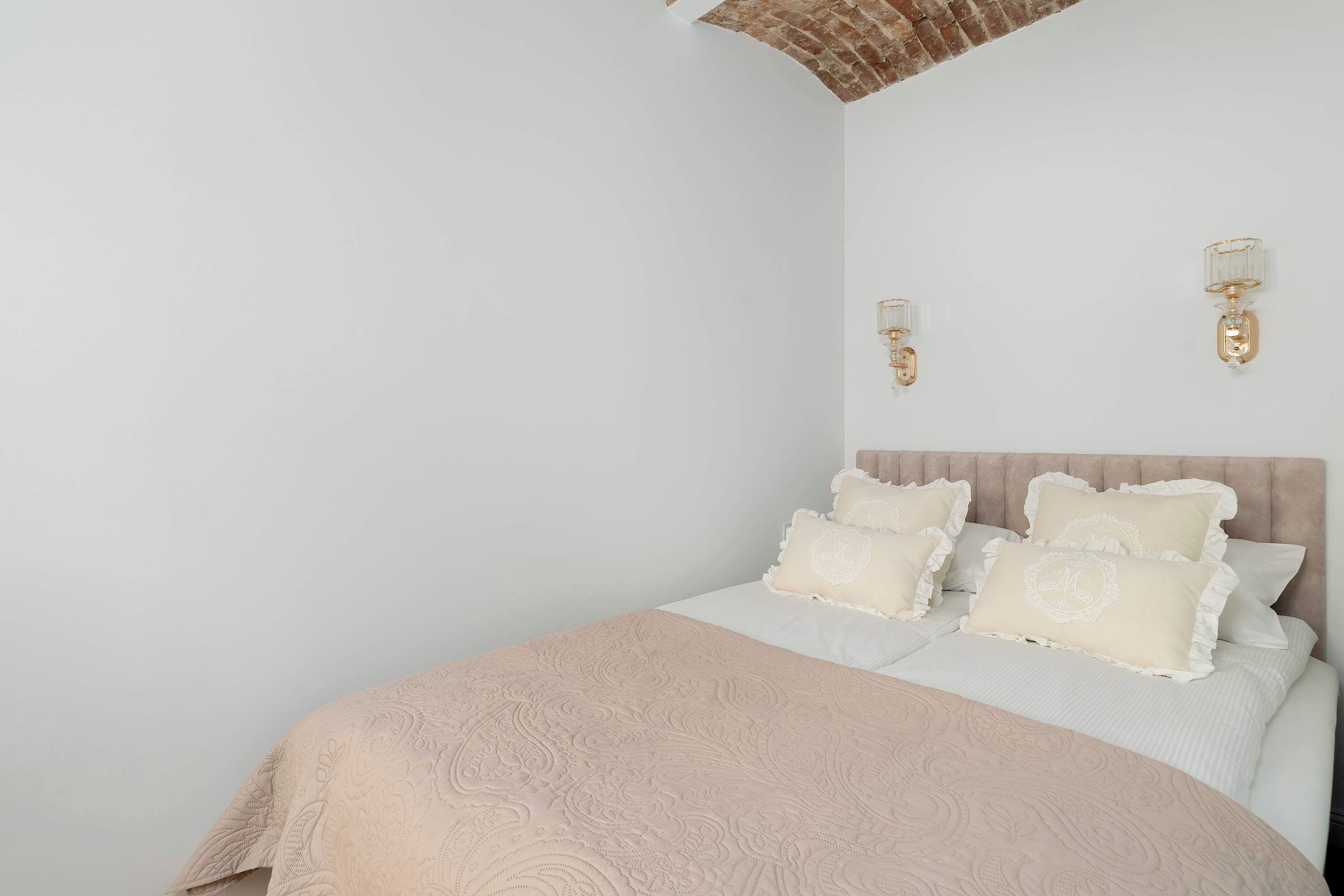 Un dormitorio con cama, paredes blancas y dos lámparas fijadas a la pared.