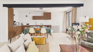A modern living room with a sofa, a dining table set for four, and a kitchen area with wooden cabinets and a radiator. - 700 m from the beach, House for 8, garden (L'Epine)