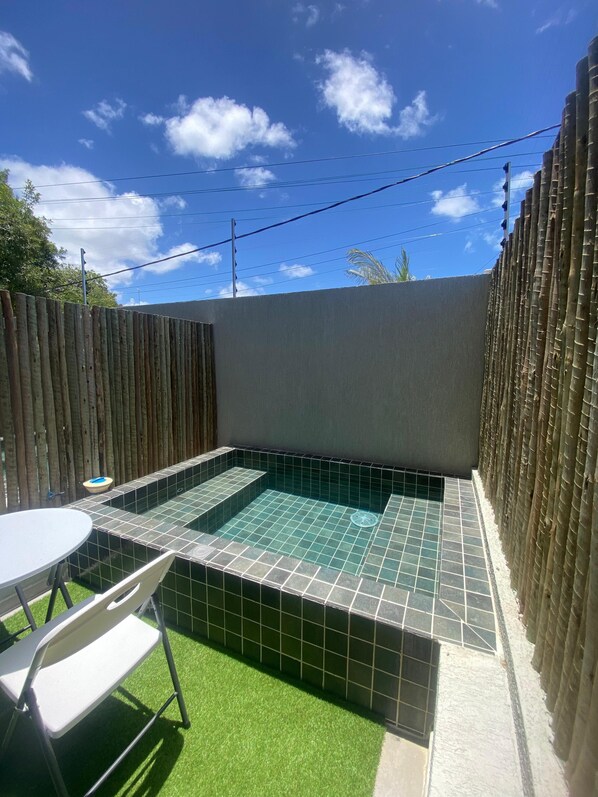 A small outdoor pool with tiled flooring, surrounded by a bamboo fence, and a white table with a chair. - Nawa 01 com piscina privativa by LP (Tamandaré)