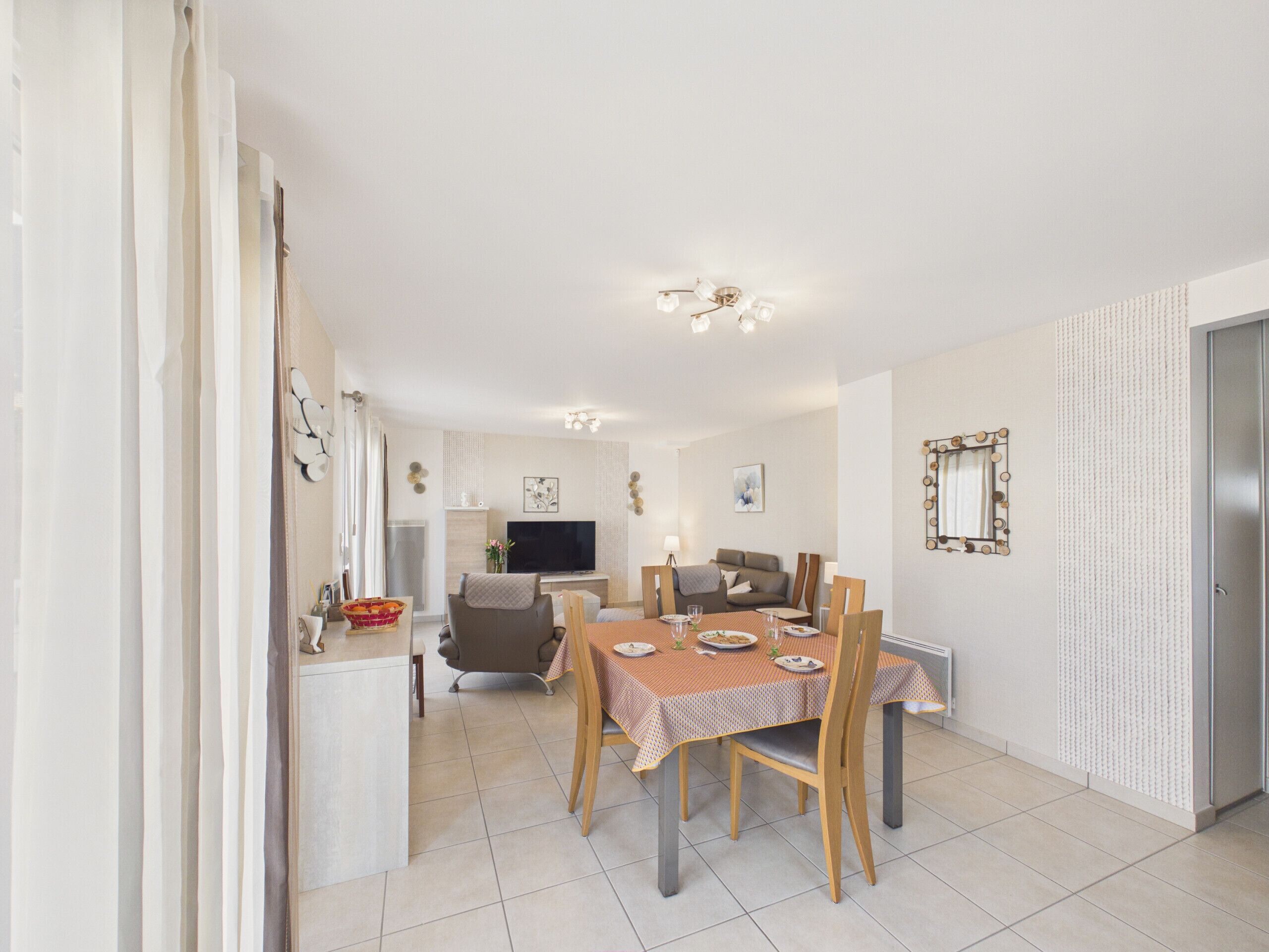 Un coin repas avec une table dressée pour quatre personnes, un canapé, un téléviseur et un miroir au mur.