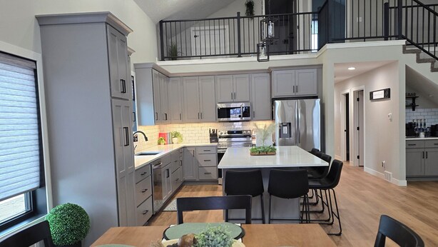 Una cocina moderna con armarios grises, una isla central y un comedor con individuales verdes y sillas negras.
