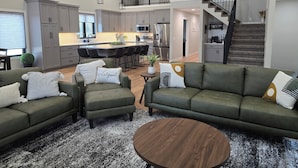Una sala de estar moderna con sofás verdes, una mesita de centro y una cocina al fondo.