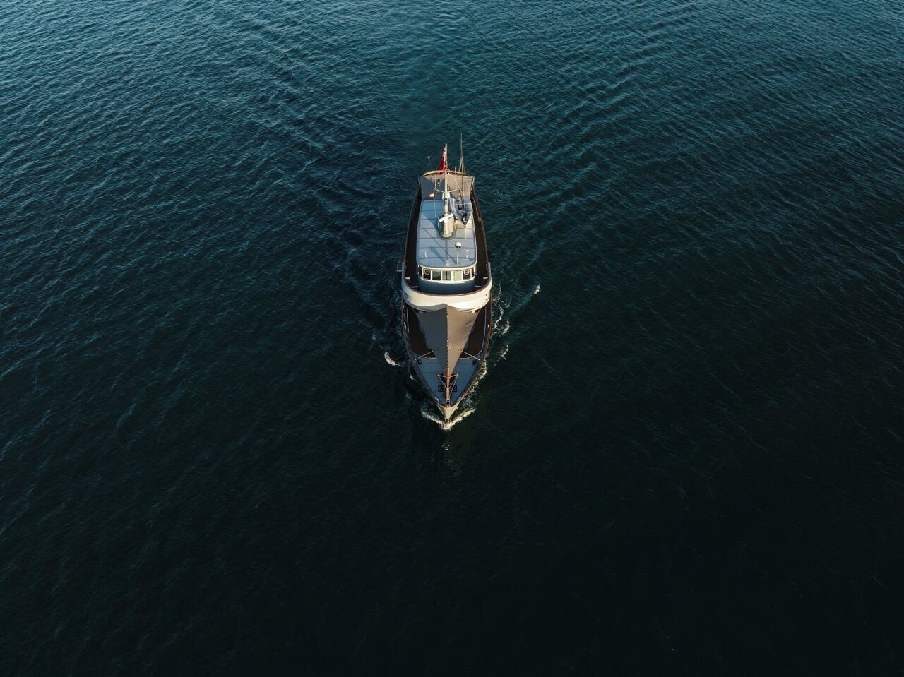 Un barco con cabina, una bandera y estela.