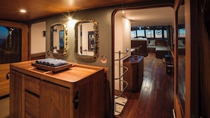 A wooden cabin interior with a wooden vanity, two mirrors, a bench, and a view through a doorway to a living area with a sofa and a table.