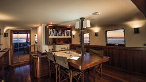 A cozy interior with a wooden table, chairs, a bookshelf, and a view through a window.