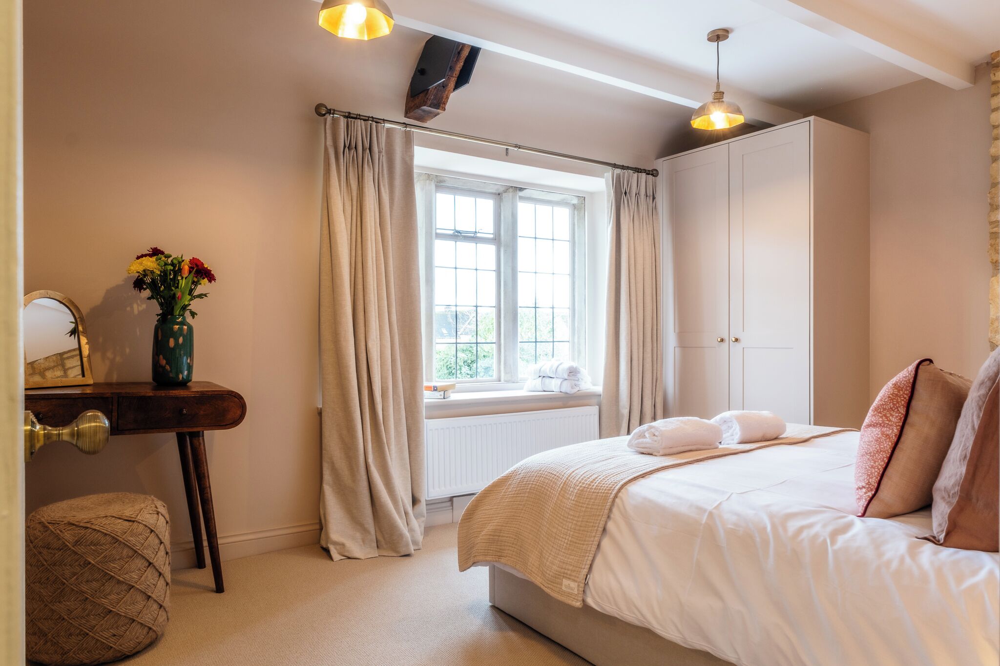 Une chambre à coucher avec un lit, une fenêtre avec des rideaux, une table de chevet avec un vase et une armoire.