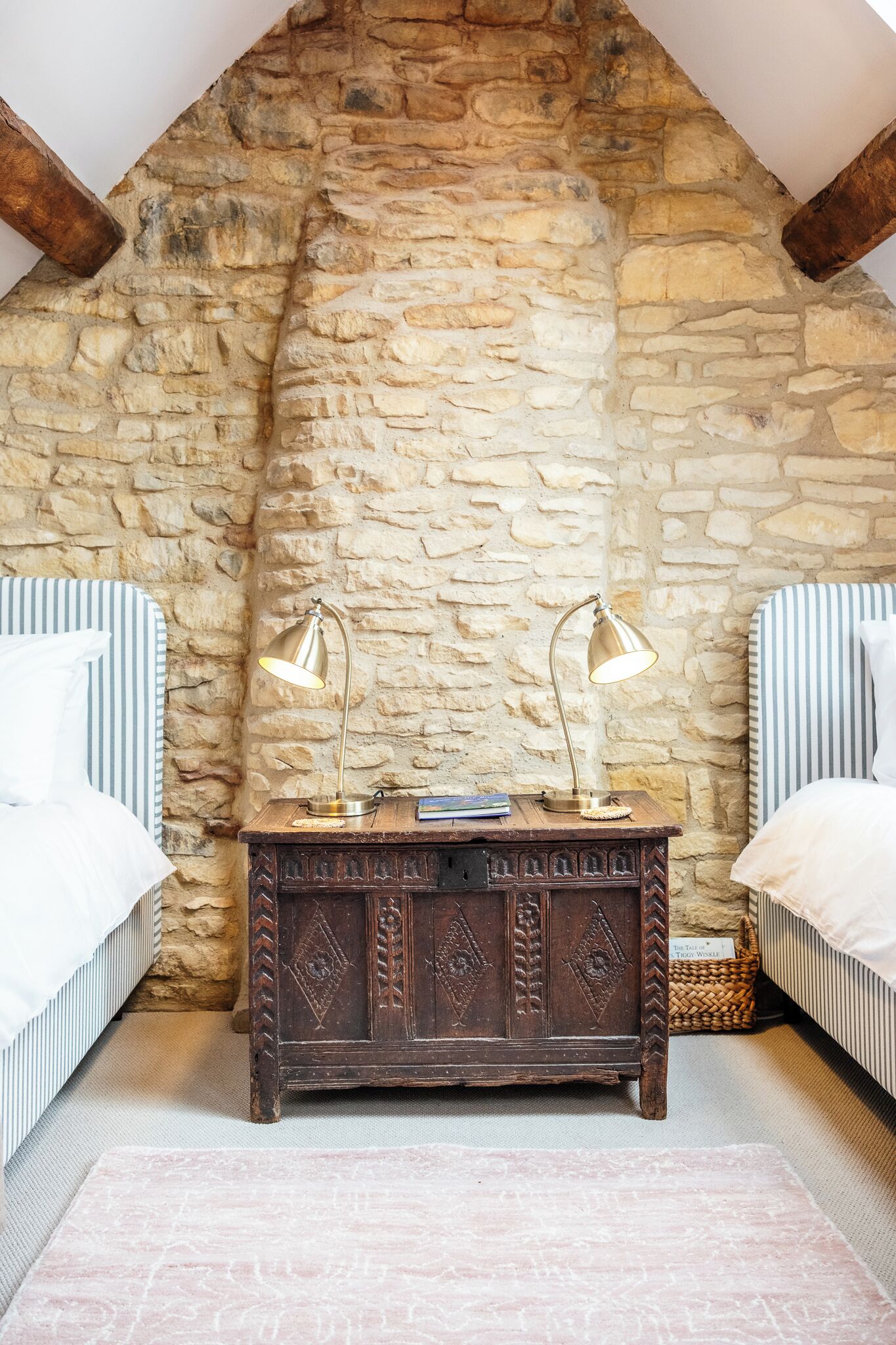 A bedroom with a stone wall, a wooden nightstand, two bedside lamps, and striped bedding.